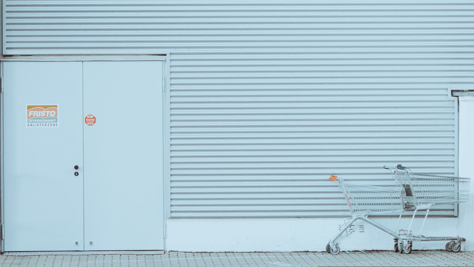 A minimalist urban setting featuring a turquoise corrugated wall and an empty shopping cart.