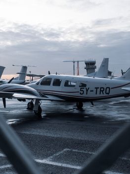 Stylish small airplane parked on a wet tarmac at dawn with an airport control tower in Kenya.