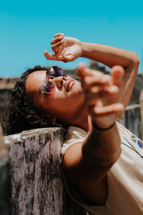 Free Man in sunglasses striking a pose outside against a textured wall under a bright sky. Stock Photo