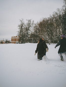 A couple playfully runs through deep snow in a winter park, showcasing joy and adventure.