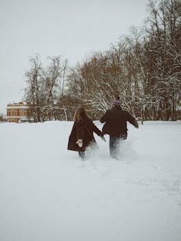 A couple walks hand in hand through a snowy landscape, surrounded by bare trees.