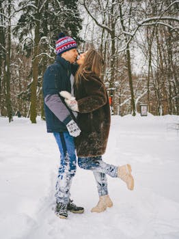 A loving couple kisses amidst a snowy winter park, showcasing romance and warmth.