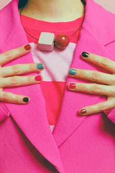 Close-up of a person in pink attire showcasing colorful nail polish and fashion jewelry.