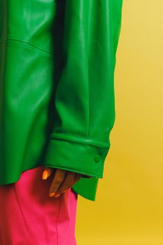 Close-up of a bold green jacket paired with vibrant pink pants, set against a yellow backdrop, showcasing modern fashion.