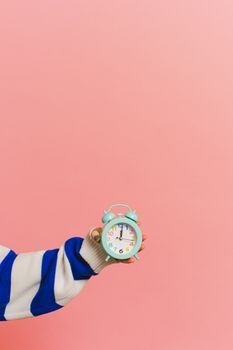 A person holding a small mint green clock in front of a pink background.