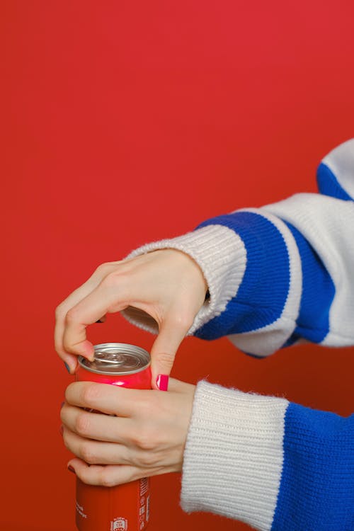 Person in Blue and White Long Sleeve Shirt Holding Can