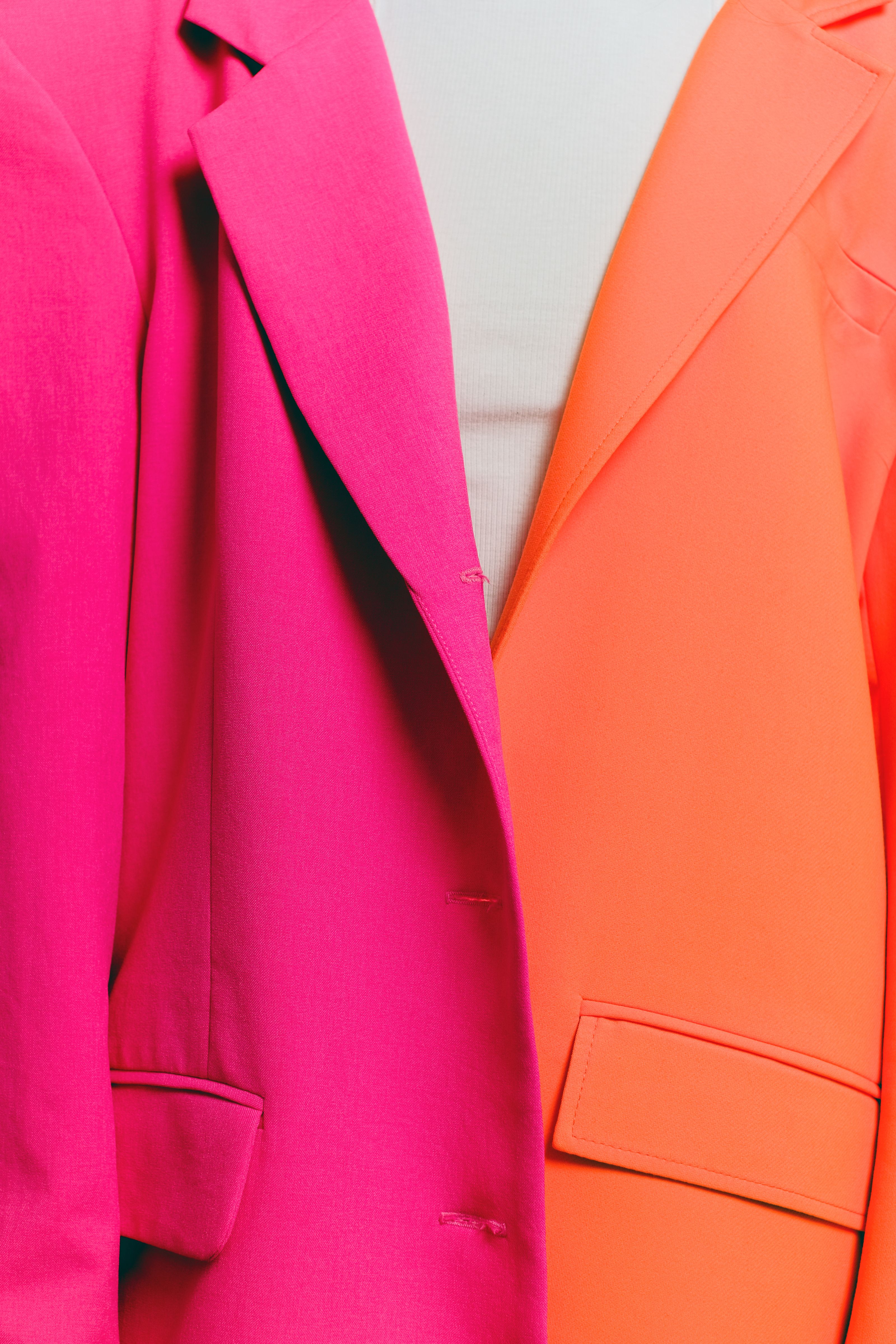 Close-up de blazers vibrantes rosa e laranja, perfeitos para uma declaração de moda ousada.