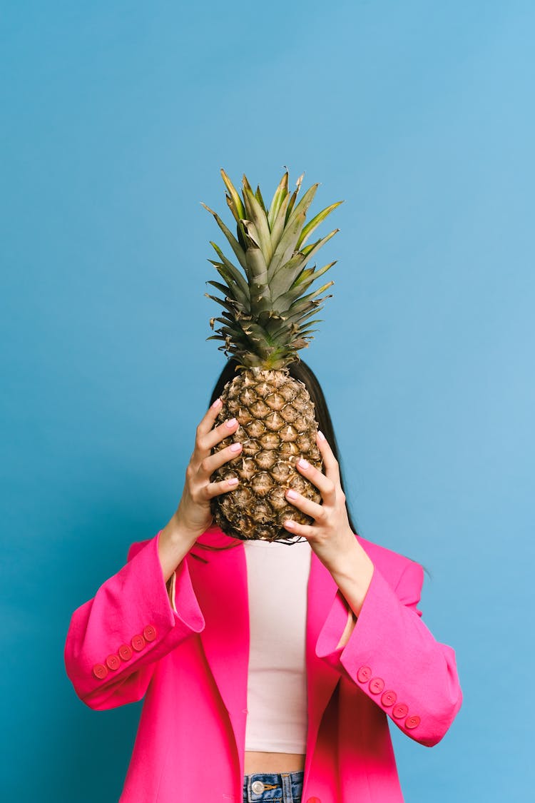 A Woman In Pink Blazer Holding A Pineapple Fruit Covering Her Face