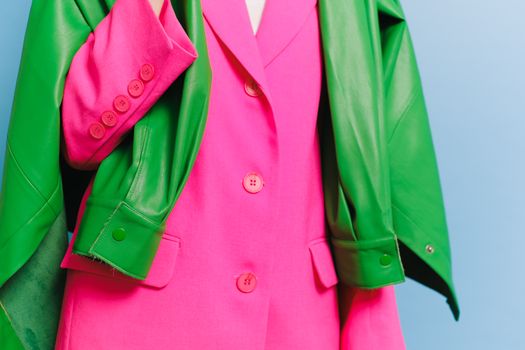 Stylish pink blazer with a contrasting green leather jacket draped over it, showcasing bold fashion colors.
