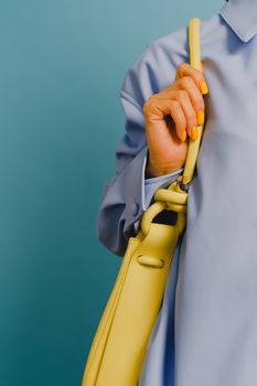 Close-up of a fashionable woman with yellow handbag against a blue background, showcasing manicure.