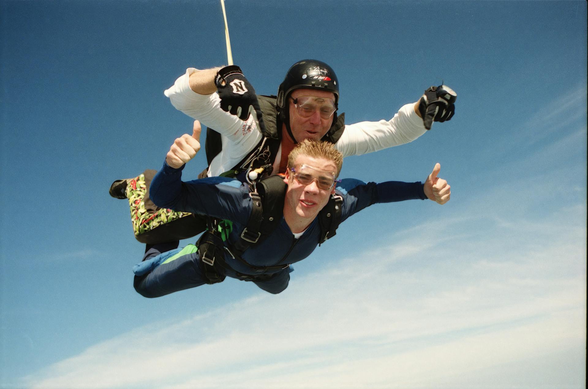 Two people tandem skydiving with thumbs up against a clear blue sky, embodying adventure and exhilaration.