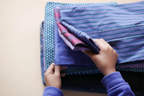 Free Hands folding a pile of colorful patterned shirts arranged neatly in a high-angle view. Stock Photo