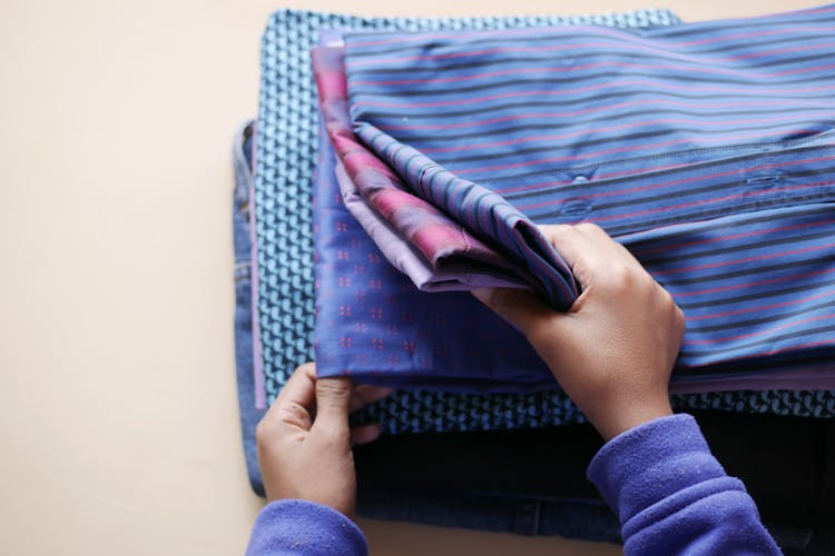 Hands Of A Person Holding A Pile Of Folded Shirts