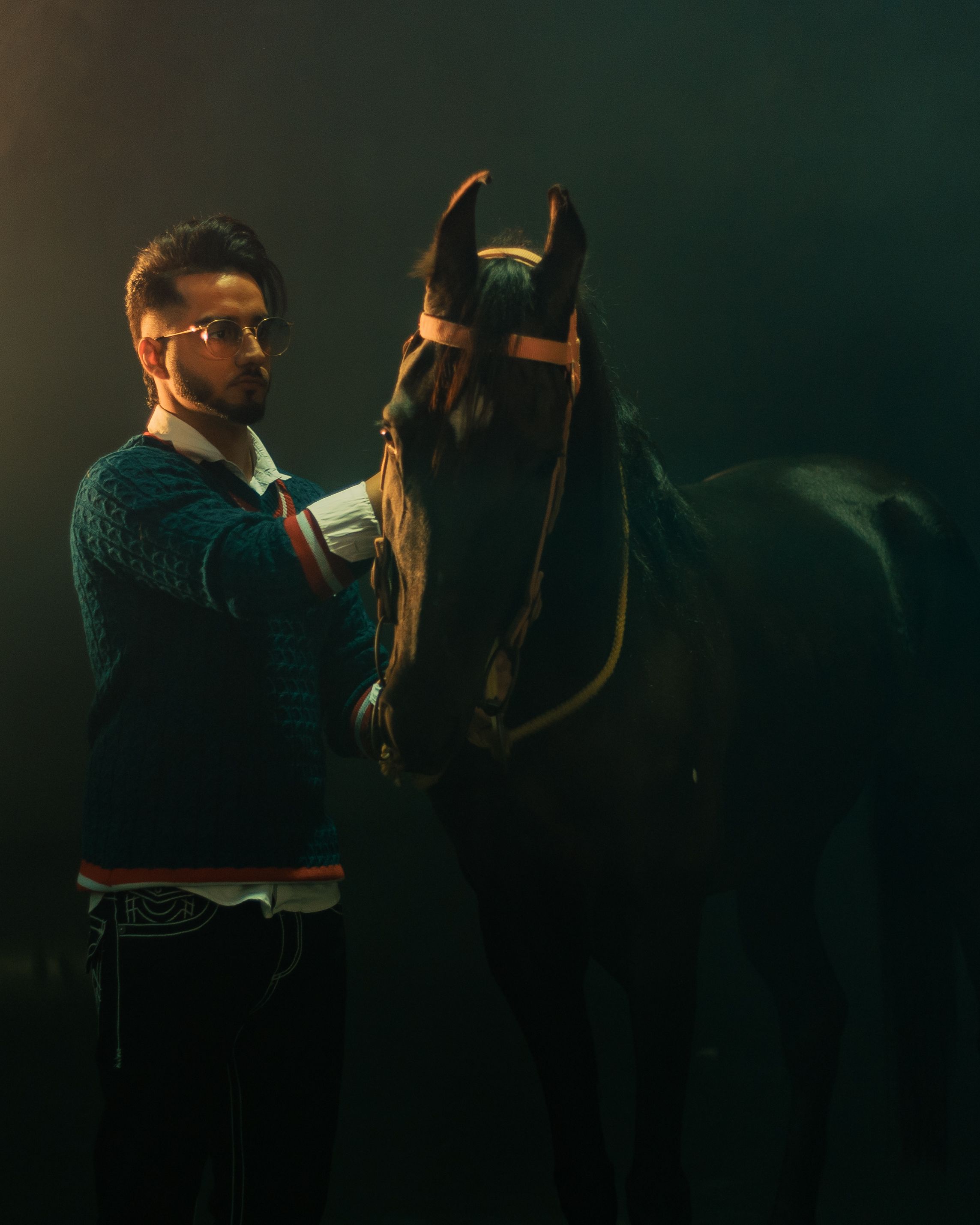 Stylish man petting a horse in a dark studio setting, exuding elegance and calm.