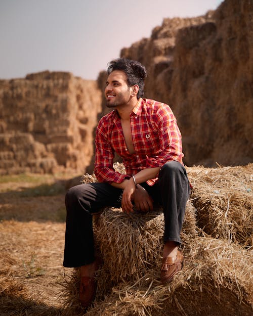 Man in Red Plaid Shirt and Black Pants Sitting on Hay Bale