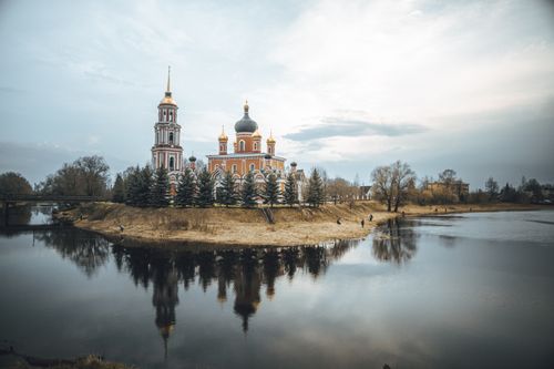 Free Scenic view of an Orthodox church reflected in a calm river with a cloudy sky backdrop. Stock Photo