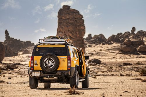 Free A bold yellow SUV navigates the challenging terrain of a rocky desert landscape under a clear sky. Stock Photo