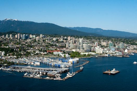 Scenic aerial view of a bustling coastal city with marina, mountains, and clear skies.