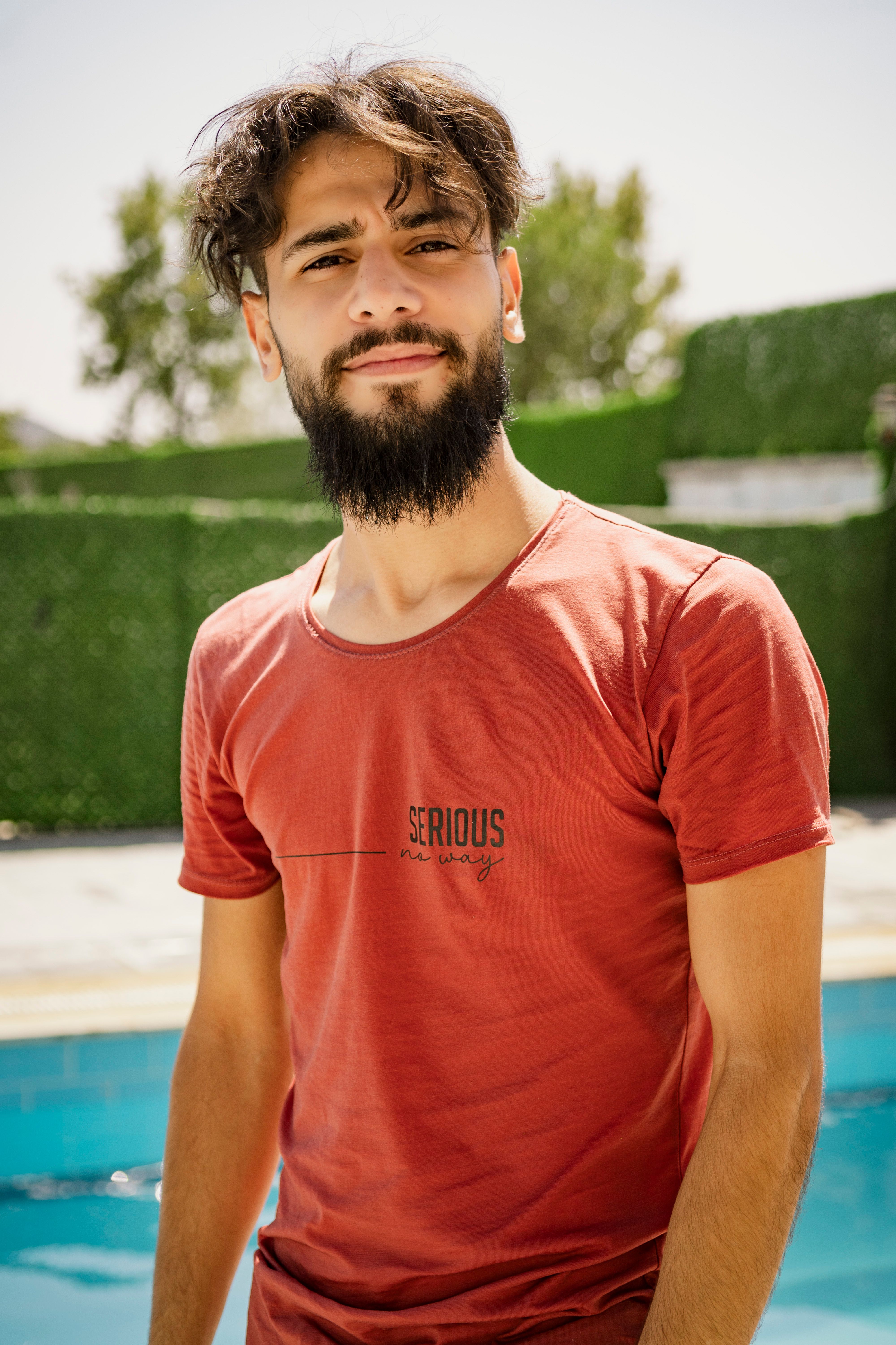 Portrait of a smiling man in a red shirt by a pool on a sunny day in Gaziantep, Turkey.