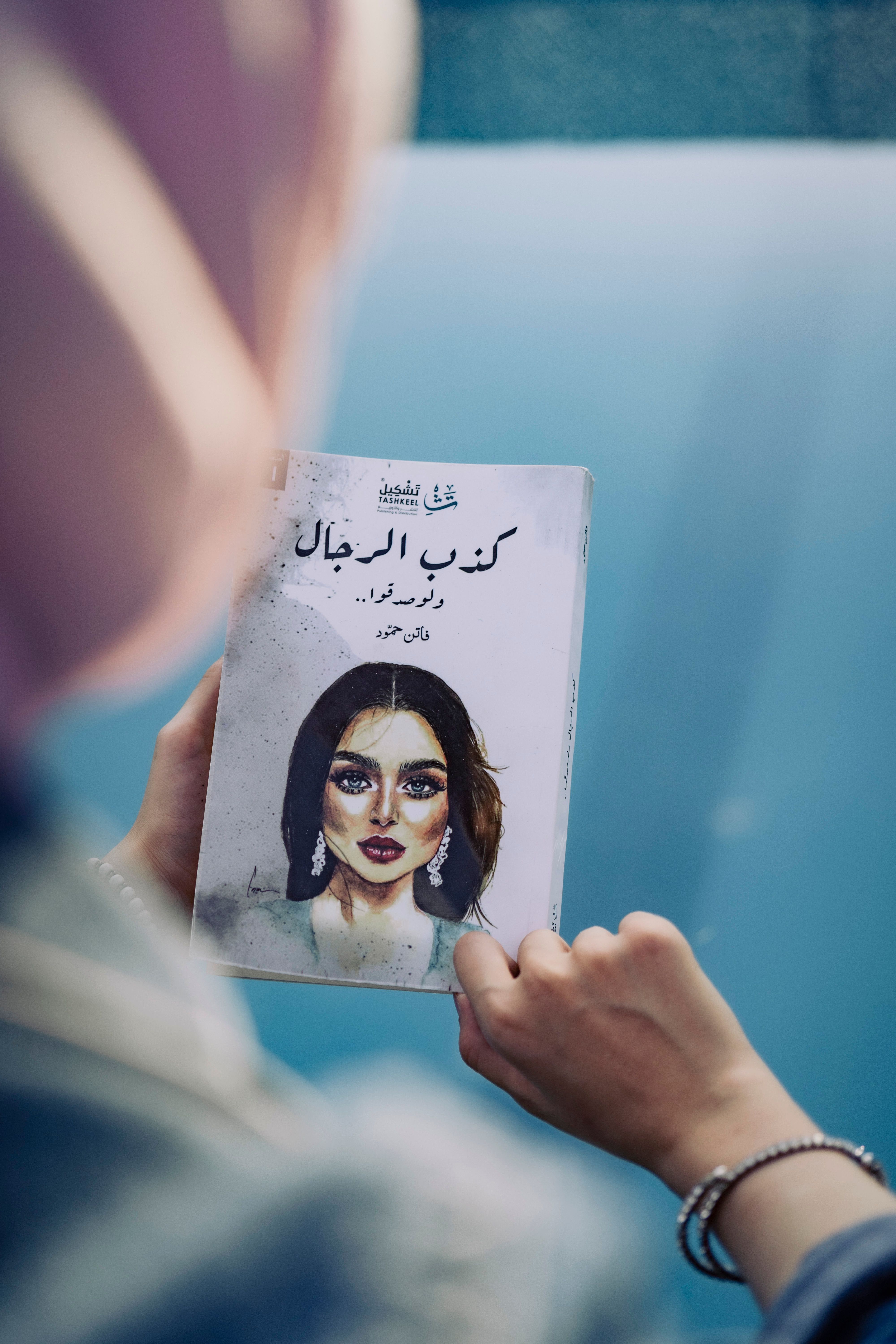 Back view of a woman holding a book featuring Arabic script and artwork.