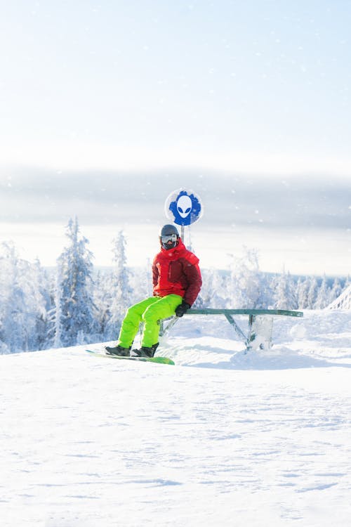 A Snowboarder Sitting on a Bench on a Snowy Mountain