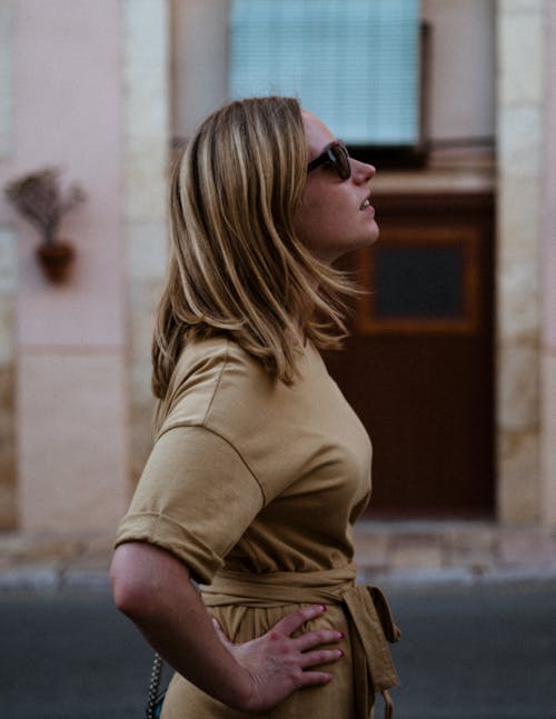 Woman in Brown Dress and Black Sunglasses Standing Near Building