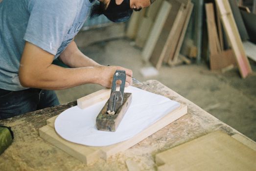 Carpenter woodworking with a hand plane on a wooden surface indoors.
