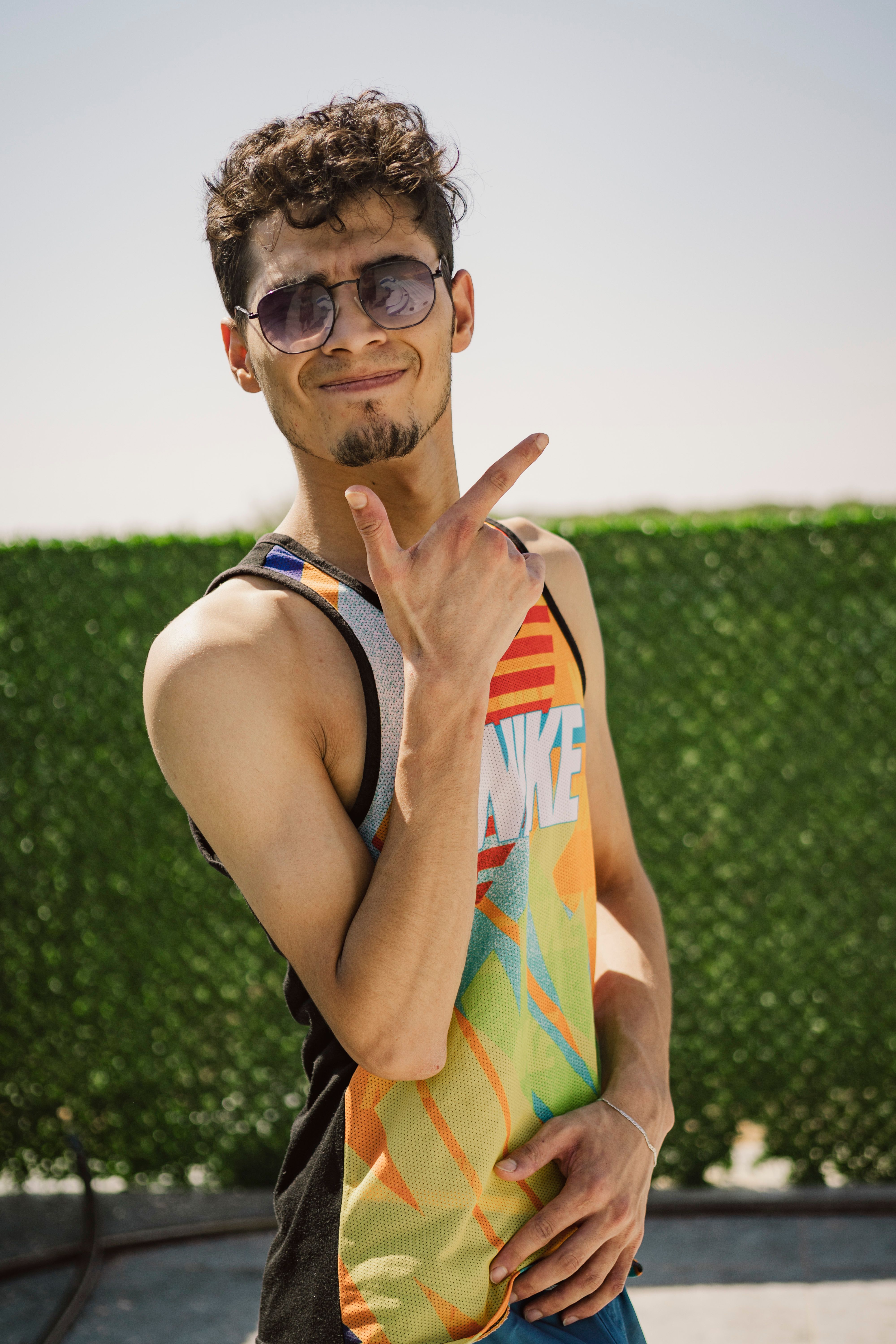 Young man wearing sunglasses and tank top posing confidently outdoors on a sunny day.