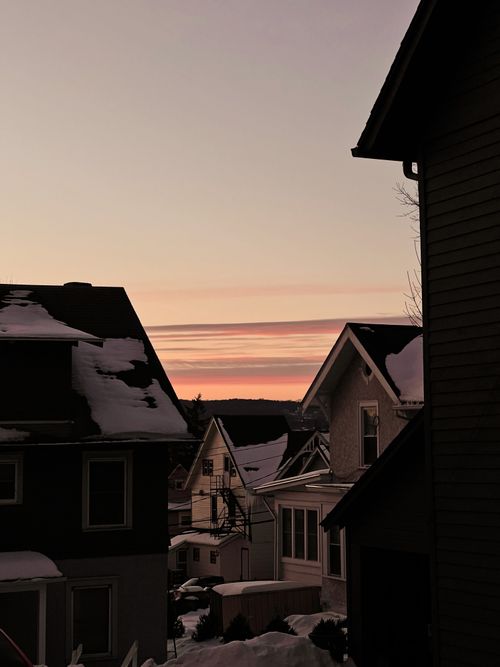 Free A serene winter sunset over a snowy urban residential area with rooftops and sky view. Stock Photo