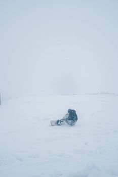 A snowboarder sits alone in a misty, snow-covered field, creating a peaceful winter scene.