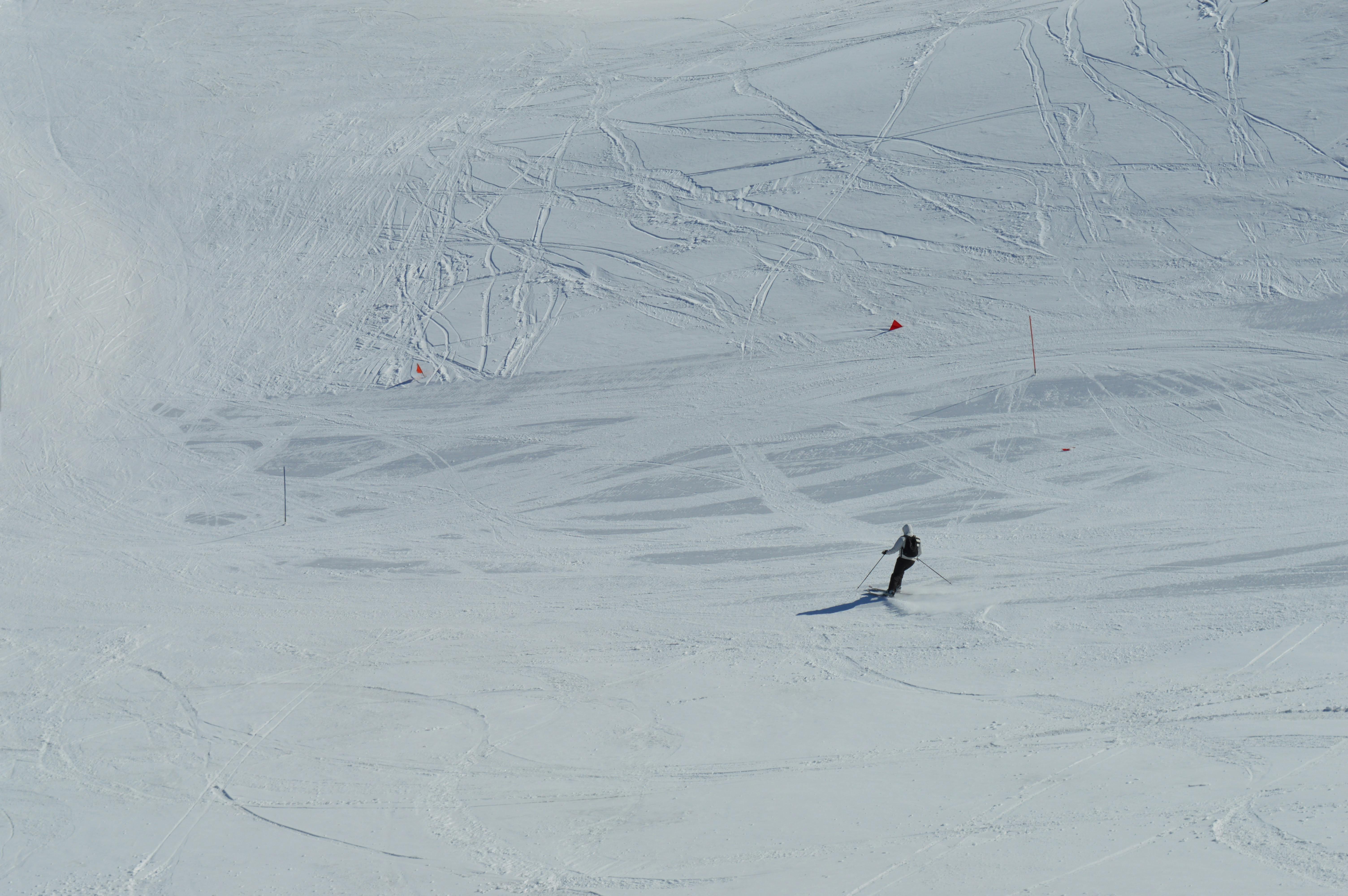 A lone skier traverses an expansive snowy landscape, leaving behind ski tracks on a sunny winter day.