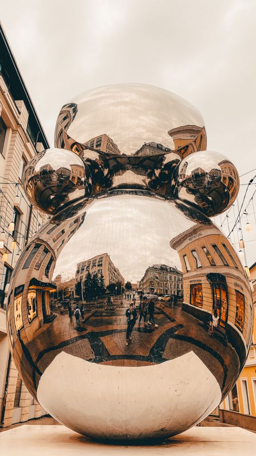 Free Modern reflective sculpture in urban setting with city architecture mirrored on surface. Stock Photo