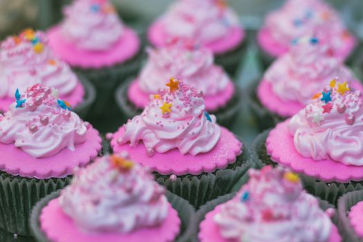 Close-up of freshly baked pink cupcakes with colorful sprinkles and frosting.