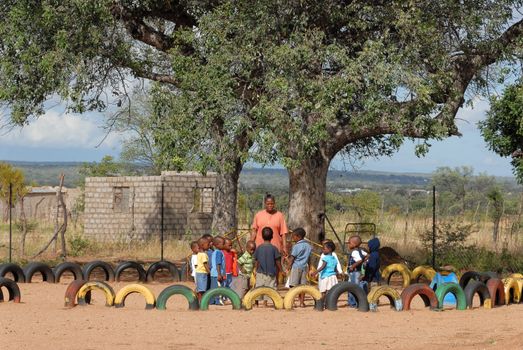Group of children playing in outdoor playground in rural South Africa under a large tree.
