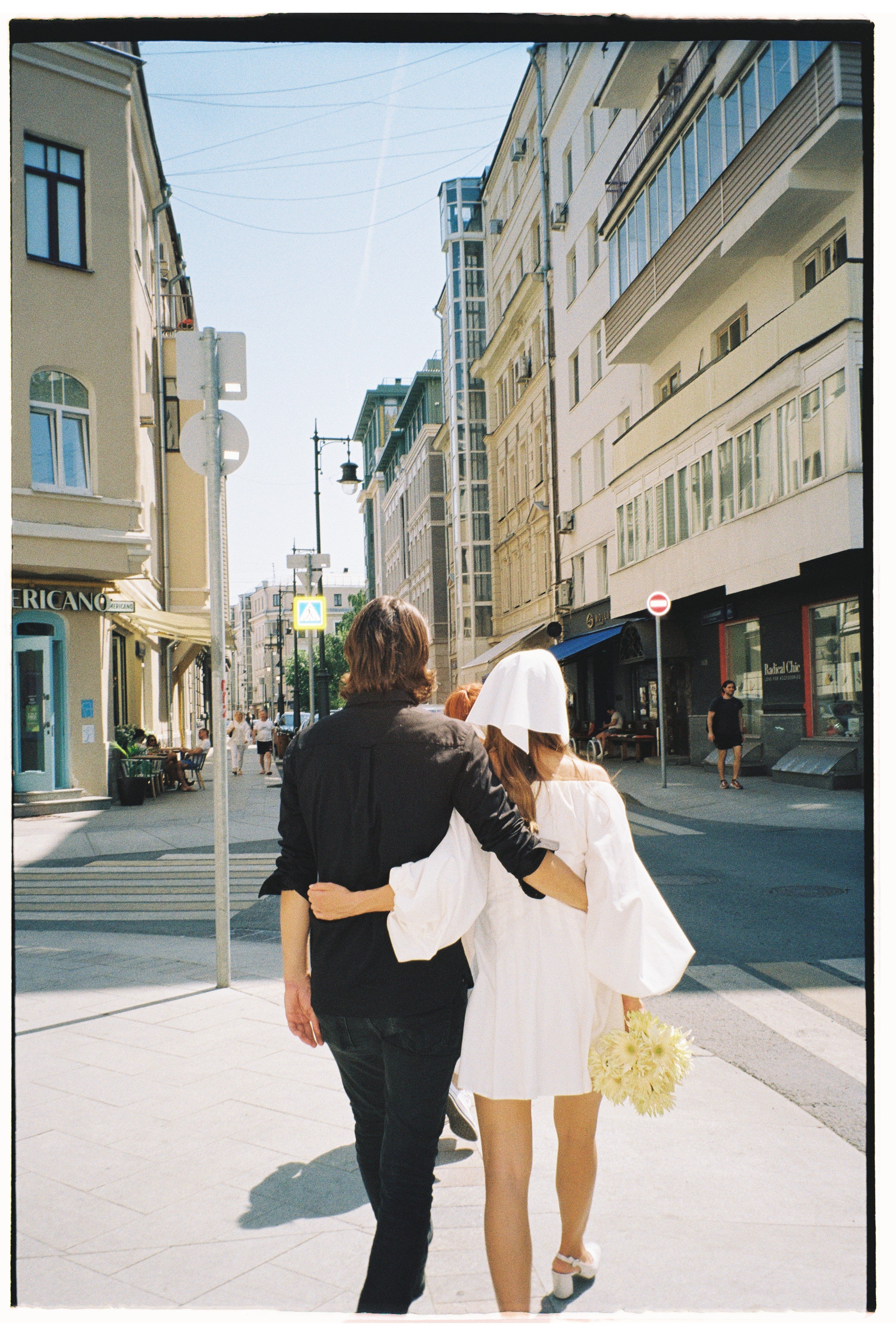 A couple walking arm in arm on a sunny city street, conveying a romantic and relaxed atmosphere.
