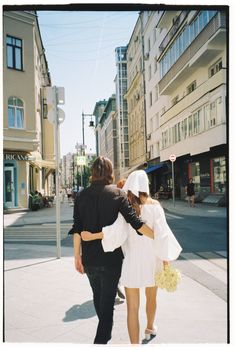A couple walking arm in arm on a sunny city street, conveying a romantic and relaxed atmosphere.