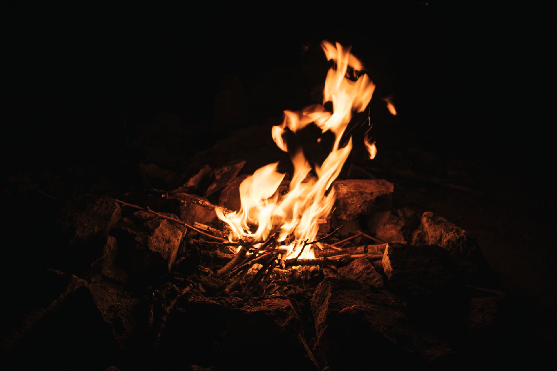 A campfire igniting sticks and stones in a dark outdoor setting, exuding warmth.