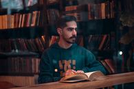 Man reading a book in a Tehran library, capturing a thoughtful moment in a cozy setting.