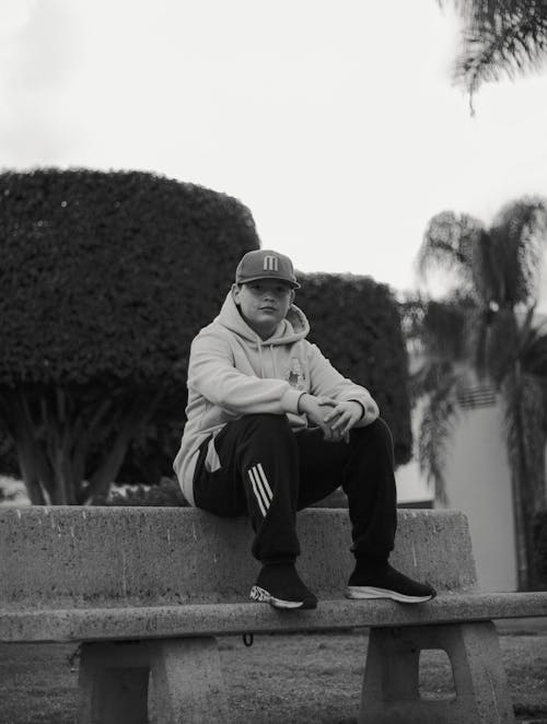 A Man in Hoodie Jacket and Black Pants Sitting on a Concrete Bench