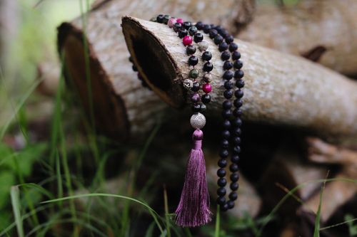 Free A handcrafted beaded necklace with tassel elegantly draped over rustic logs, surrounded by natural grass. Stock Photo