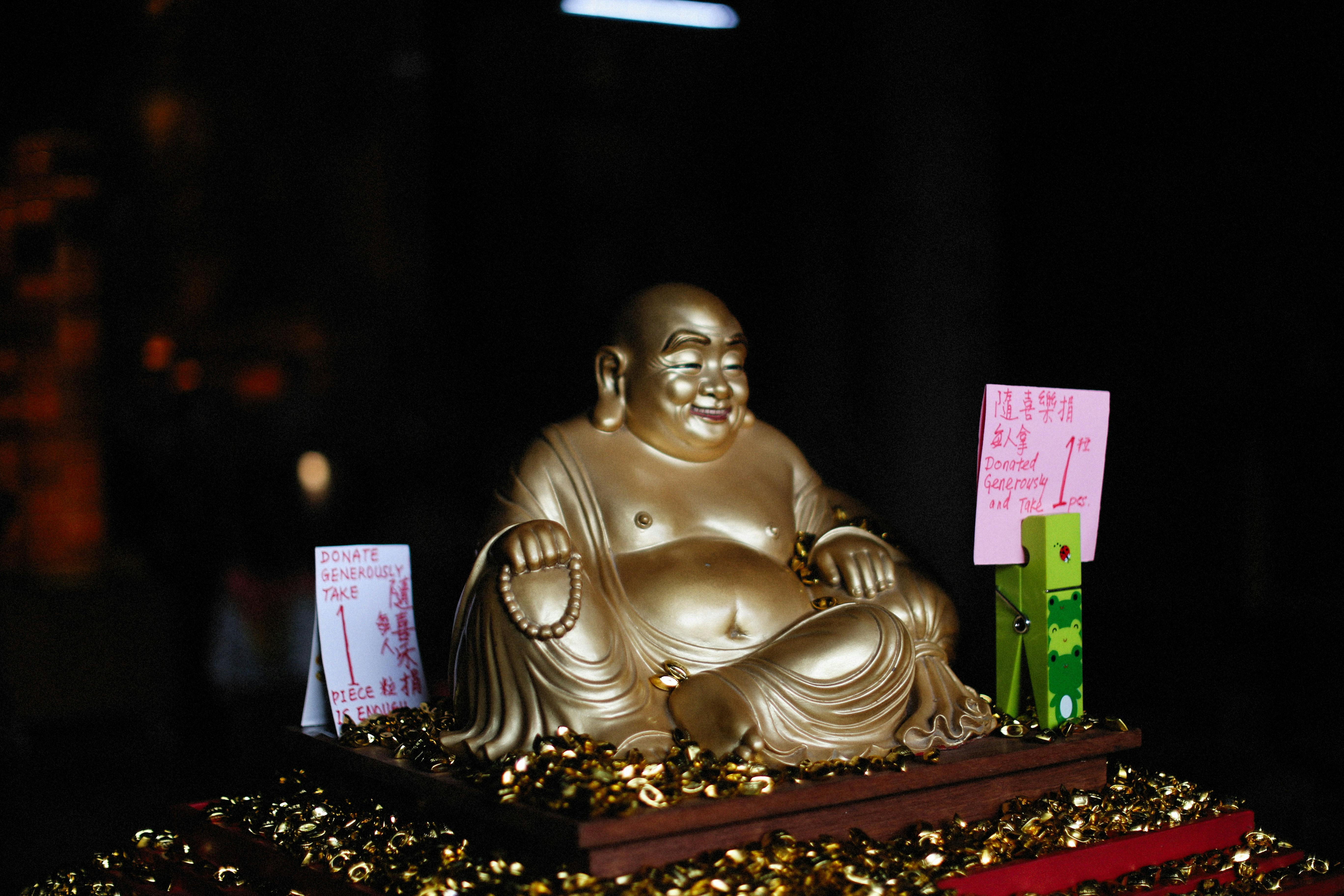 Gold Laughing Buddha statue adorned with donation signs and coins, symbolizing prosperity.