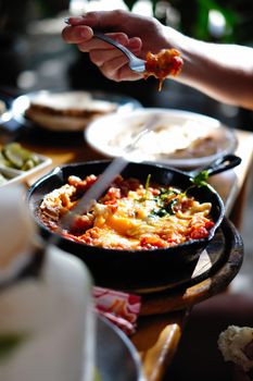 Tasty shakshuka with peppers and tomatoes in a skillet, a fork lifting a bite.