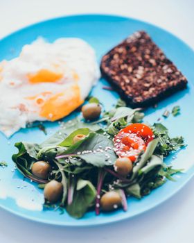 A vibrant blue plate with eggs, green salad, and dark bread for a nutritious meal.