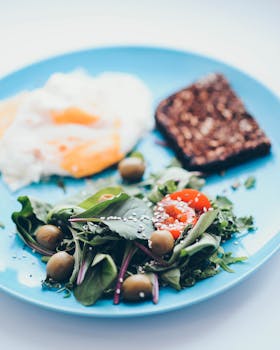 A nutritious breakfast featuring eggs, greens, olives, and whole grain bread on a blue plate.