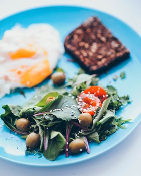 Close-up of a nutritious breakfast featuring poached eggs, mixed salad, and whole grain bread.