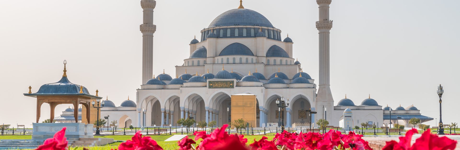 Capturing the elegance of Sharjah Mosque surrounded by vibrant red flowers during daylight.