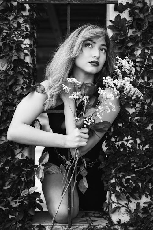 A Grayscale Photo of a Woman Looking Up while Holding Flowers
