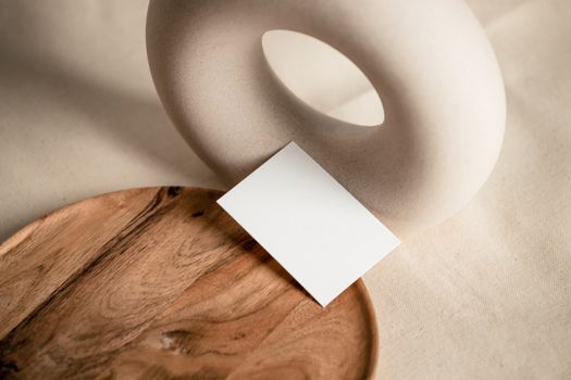 Elegant still life featuring a ceramic sculpture and wooden plate with a blank card, showcasing minimalist design.
