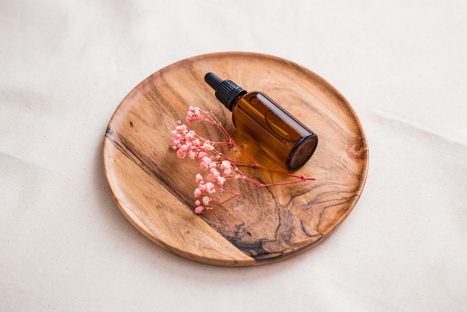 A dark glass dropper bottle of homemade aromatic bitters surrounded by star anise, cinnamon sticks, cardamom pods, and dried orange peel on a wooden board.