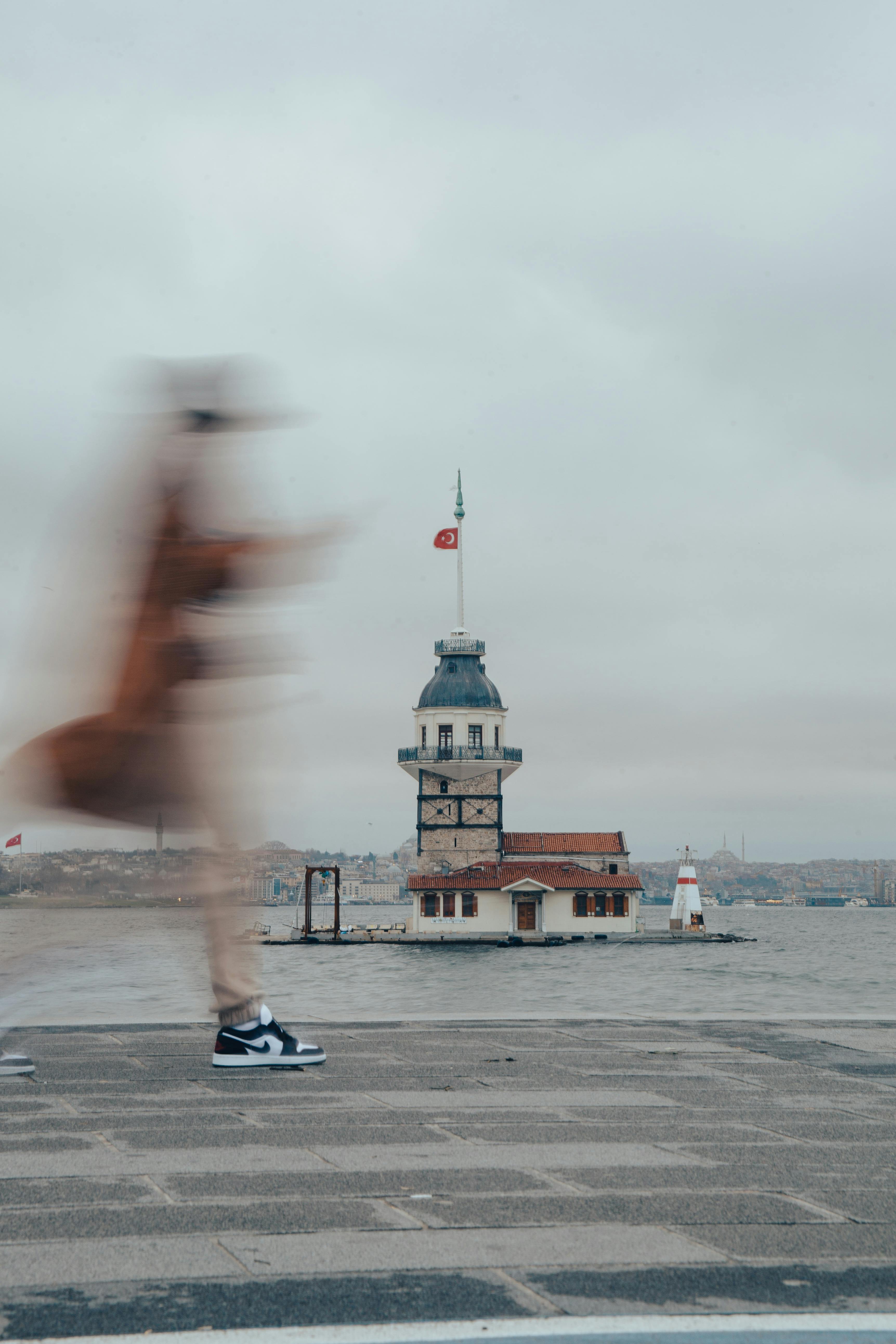 A blurred person walks near the Maiden's Tower in Istanbul, Turkey, capturing a sense of urban movement.